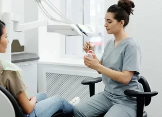 Jak bezboleśnie uzupełnić brakujące zęby w dorosłym życiu Dentystka wyjaśnia dorosłej pacjentce zabieg, trzymając model szczęki.