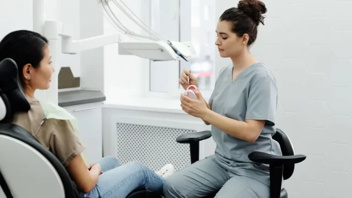 konsultacja-bezbolesne-uzupelnianie-zebow Dentystka wyjaśnia dorosłej pacjentce zabieg, trzymając model szczęki.